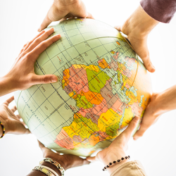 Many human hands holding a globe that displays a map of planet earth