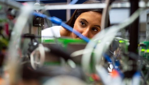 Female engineer peering into a box of wires and circuitry